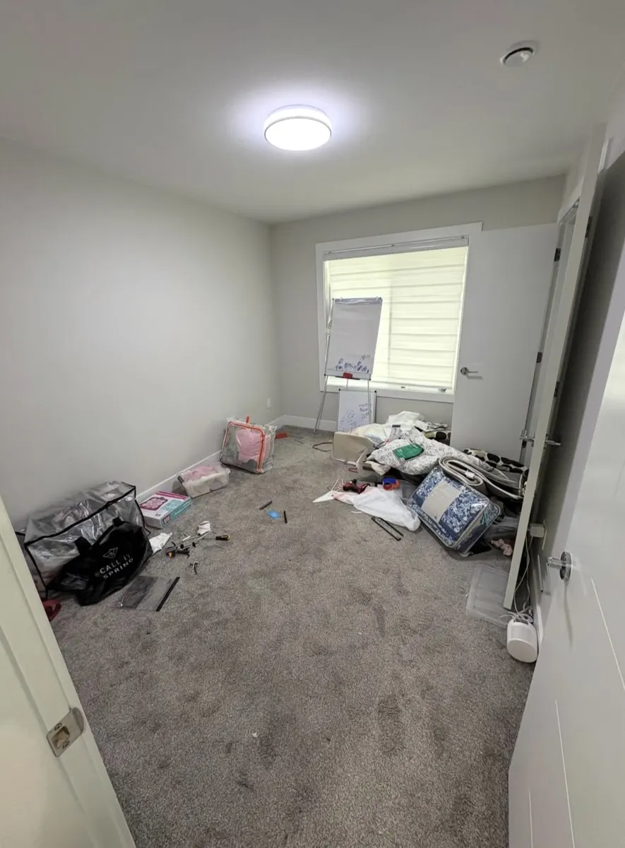 Spare room with bags, bedding and leftover items on the carpet