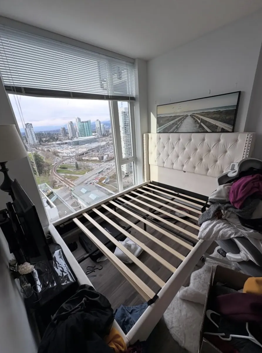 Condo bedroom with bed frame, TV and clothing before removal